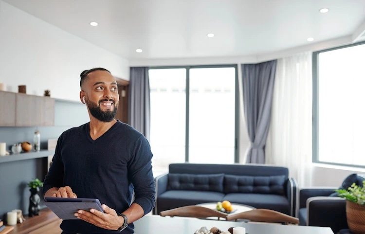 Homme souriant tenant une tablette dans un salon moderne et clair