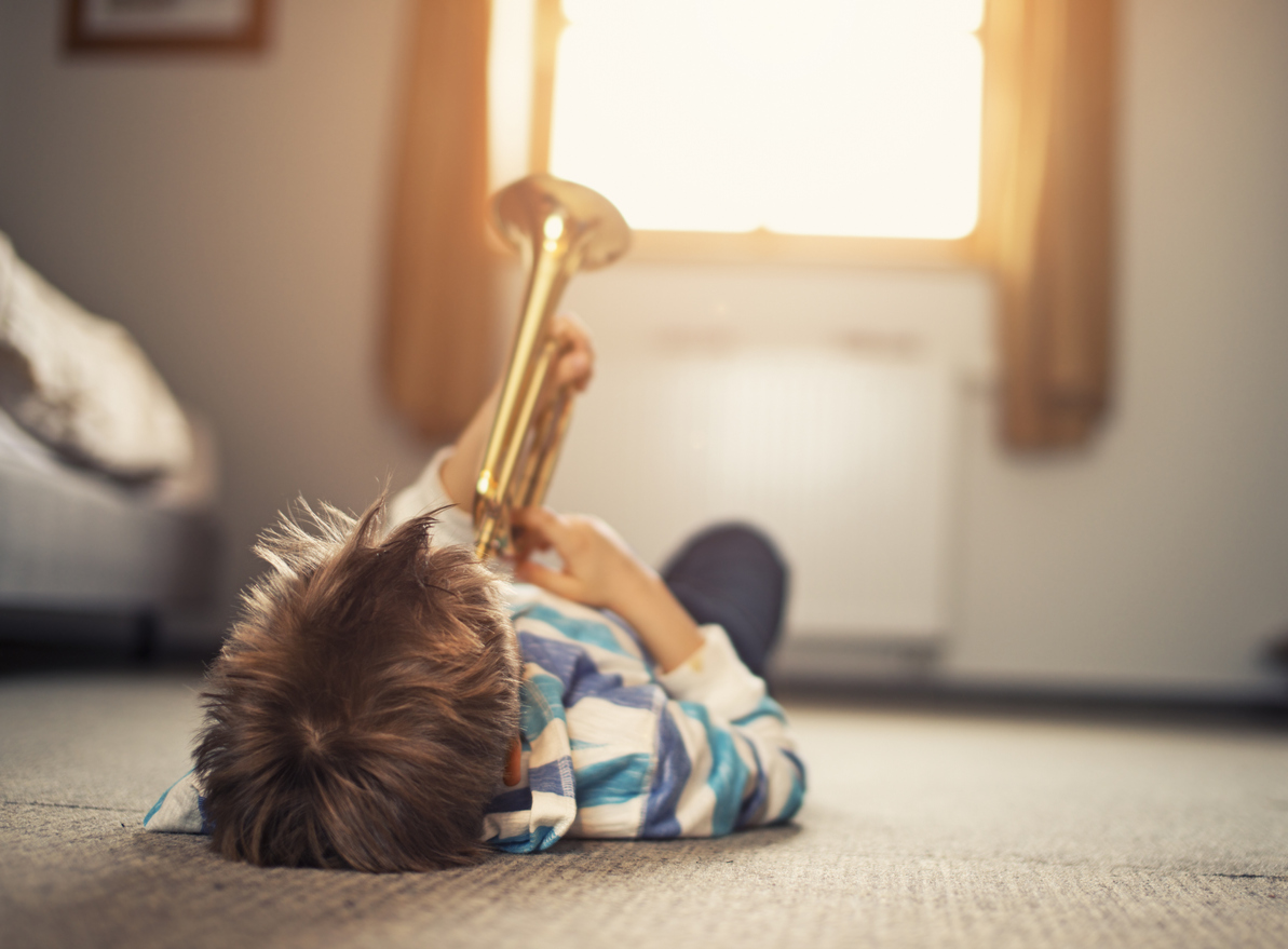 Enfant allongé sur le sol jouant avec une trompette dorée