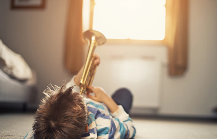 Enfant allongé sur le sol jouant avec une trompette dorée