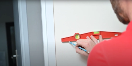 Technicien en rouge utilisant un niveau à bulle pour tracer une ligne