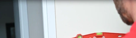 Technicien en rouge utilisant un niveau à bulle pour tracer une ligne