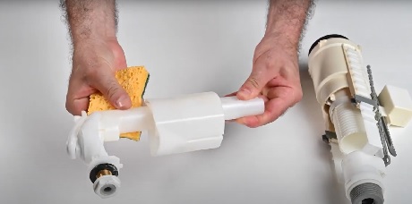 Mains tenant le mécanisme de chasse d'eau d'une toilette démontée