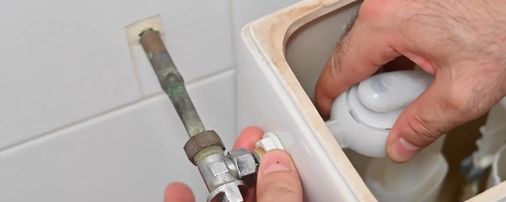 Mains remplaçant le robinet d'arrêt d'un réservoir de toilettes