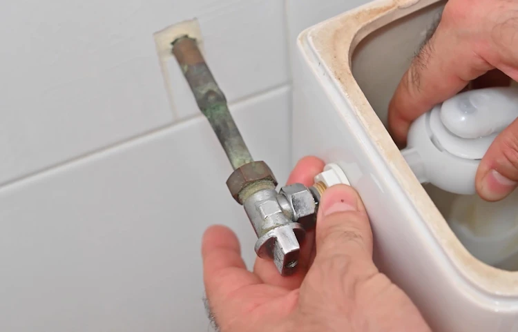 Mains remplaçant le robinet d'arrêt d'un réservoir de toilettes