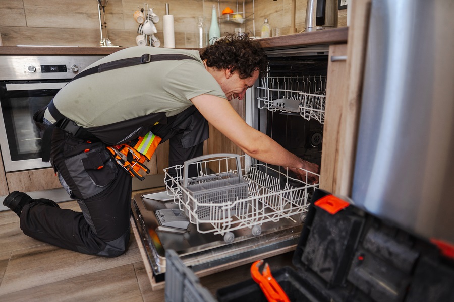 Technicien agenouillé inspectant le panier d'un lave-vaisselle ouvert