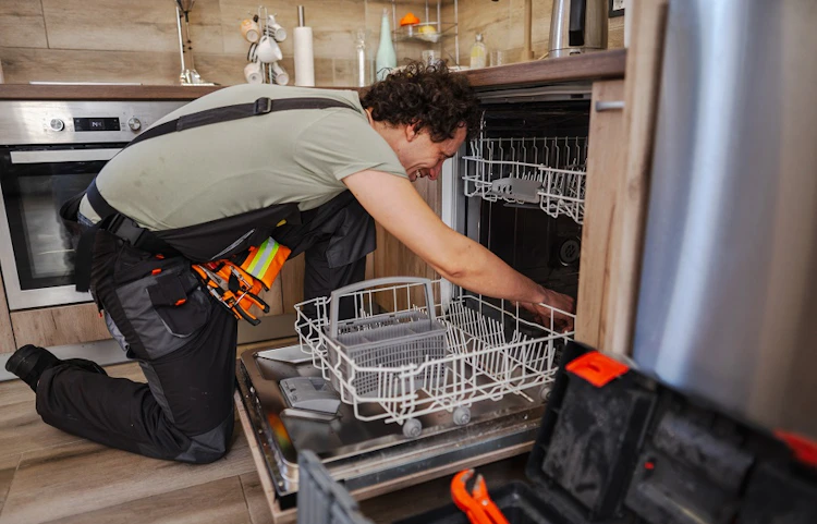 Technicien agenouillé inspectant le panier d'un lave-vaisselle ouvert