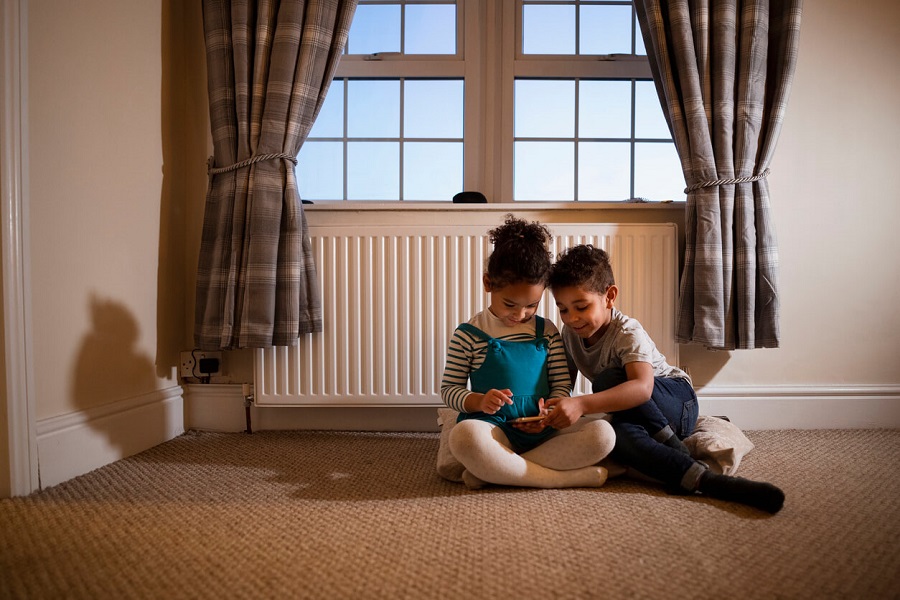 Deux enfants assis par terre devant un radiateur jouant avec une tablette