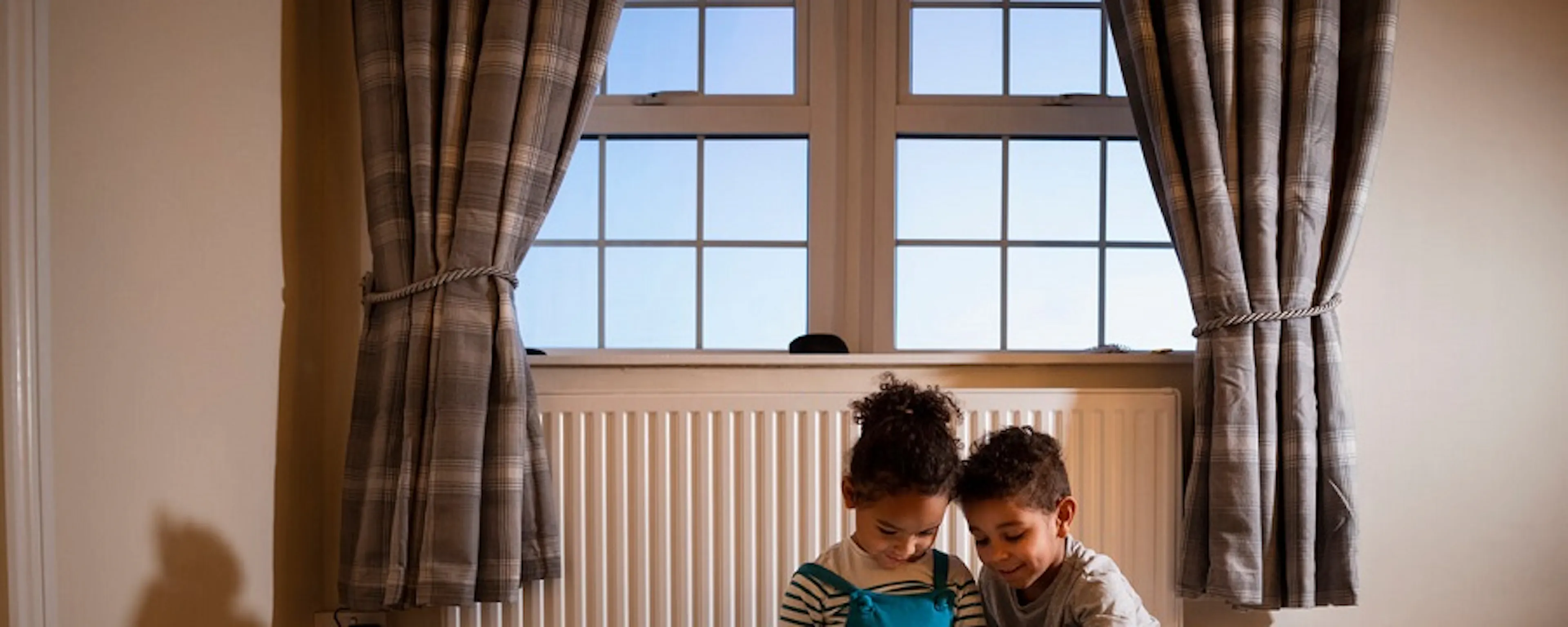 Deux enfants assis par terre devant un radiateur jouant avec une tablette