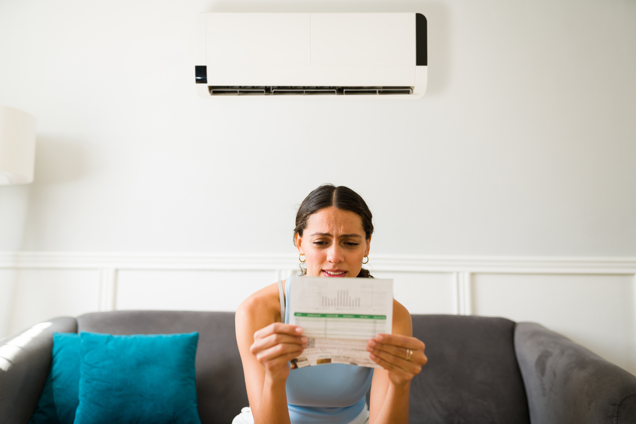Combien coûte en électricité une nuit de climatisation, se demande une jeune femme, facture en main, sur son canapé