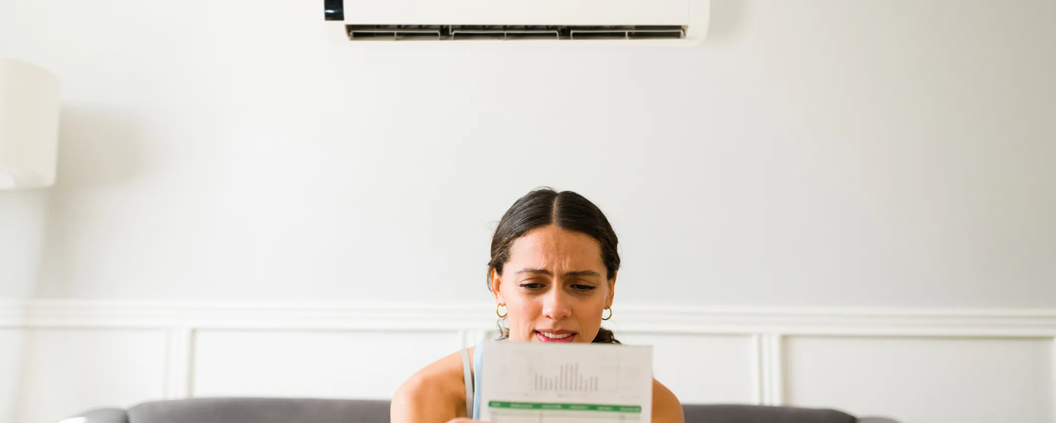 Combien coûte en électricité une nuit de climatisation, se demande une jeune femme, facture en main, sur son canapé