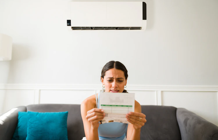 Combien coûte en électricité une nuit de climatisation, se demande une jeune femme, facture en main, sur son canapé