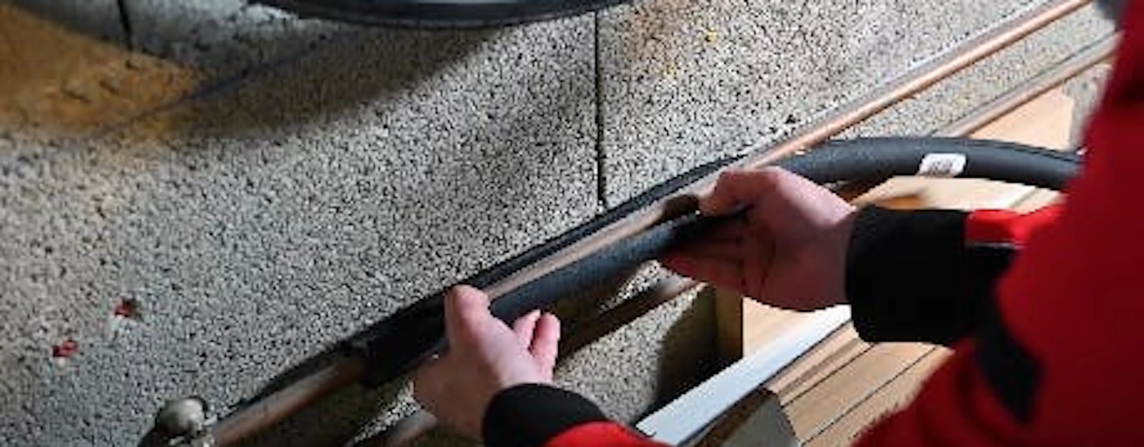 Mains en vêtement rouge travaillant sur un câble longeant un mur en béton