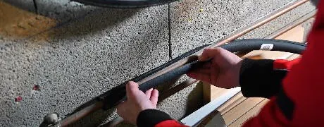 Mains en vêtement rouge travaillant sur un câble longeant un mur en béton
