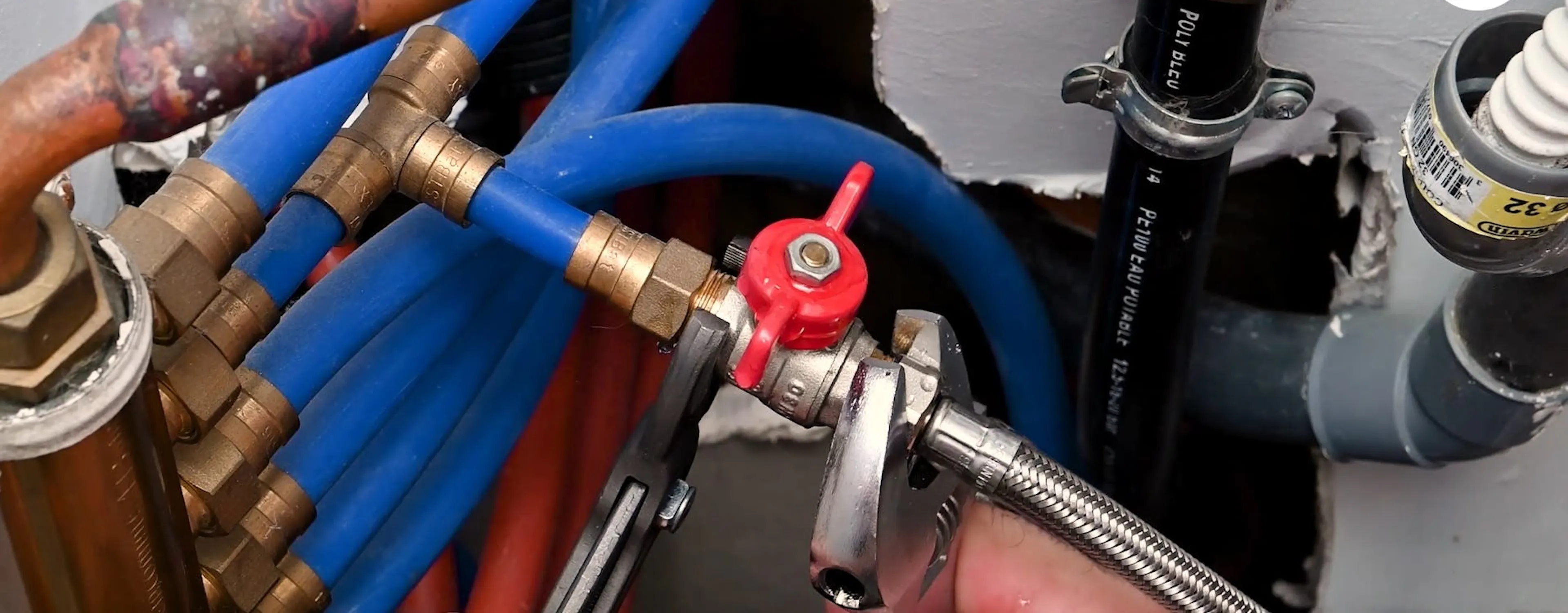 Réseau de tuyaux bleus et cuivrés avec robinet d'arrêt général rouge qui est en train d'être changé
