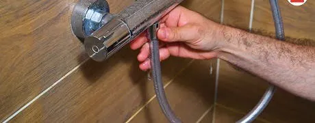 Main tenant le flexible d'un robinet mitigeur de douche chromé