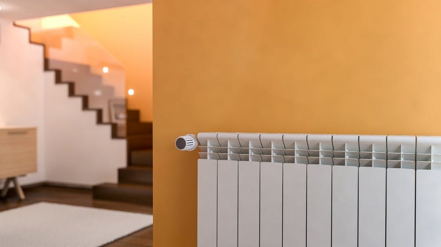 Radiateur blanc fixé sur un mur orange dans un couloir avec escalier