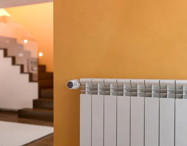 Radiateur blanc fixé sur un mur orange dans un couloir avec escalier