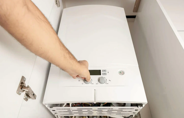 Technicien réglant le bouton de commande d'une chaudière murale blanche