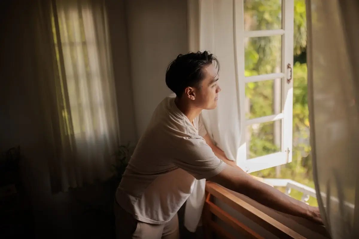 Femme pensive regardant par une fenêtre ouverte depuis l'intérieur