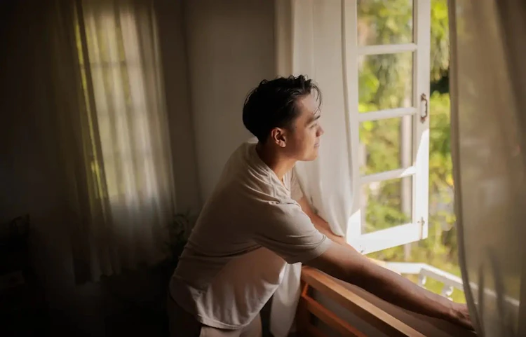 Femme pensive regardant par une fenêtre ouverte depuis l'intérieur