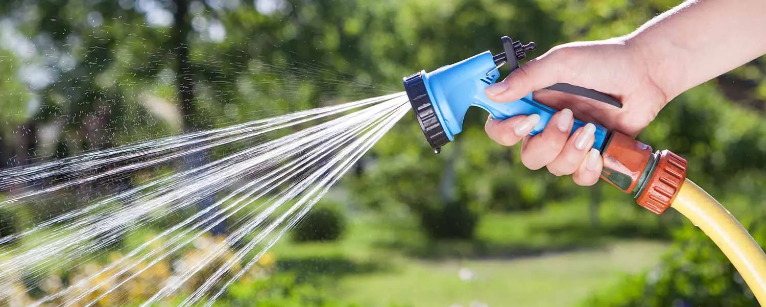 Main tenant un pistolet d'arrosage écologique pour limiter la consommation d'eau dans un jardin