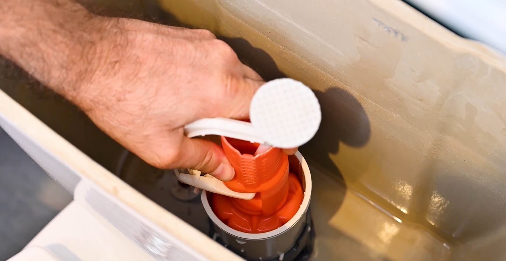 Main tenant le mécanisme de chasse d'eau à l'intérieur d'un réservoir WC