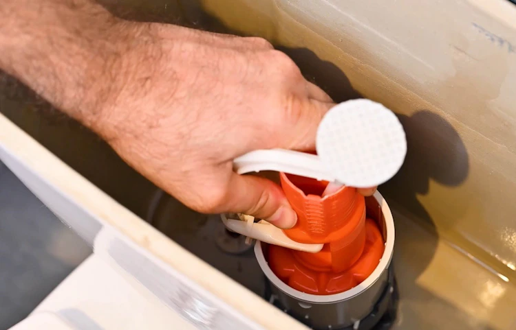 Main tenant le mécanisme de chasse d'eau à l'intérieur d'un réservoir WC