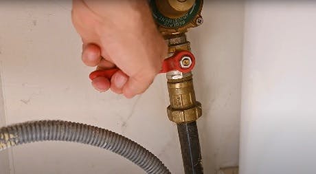 Main fermant un robinet d'arrêt sur un flexible de tuyauterie