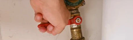 Main fermant un robinet d'arrêt sur un flexible de tuyauterie