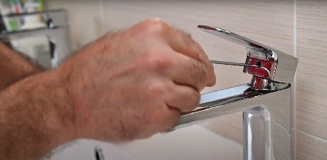 Mains serrant le bec d'un robinet de salle de bain chromé