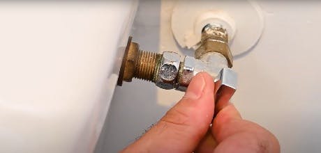 Main resserrant le raccord d'un robinet d'arrêt sous une baignoire