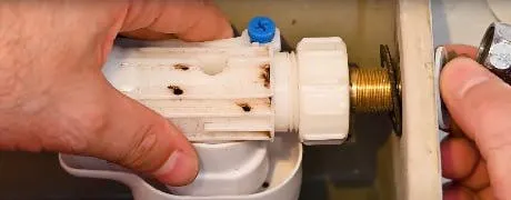 Mains démontant le mécanisme de remplissage d'un réservoir WC