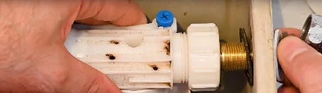 Mains démontant le mécanisme de remplissage d'un réservoir WC