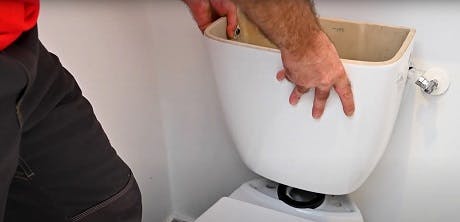 Main soulevant le couvercle d'un réservoir de chasse d'eau WC