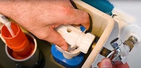 Mains manipulant le mécanisme de chasse d'eau dans un réservoir WC ouvert