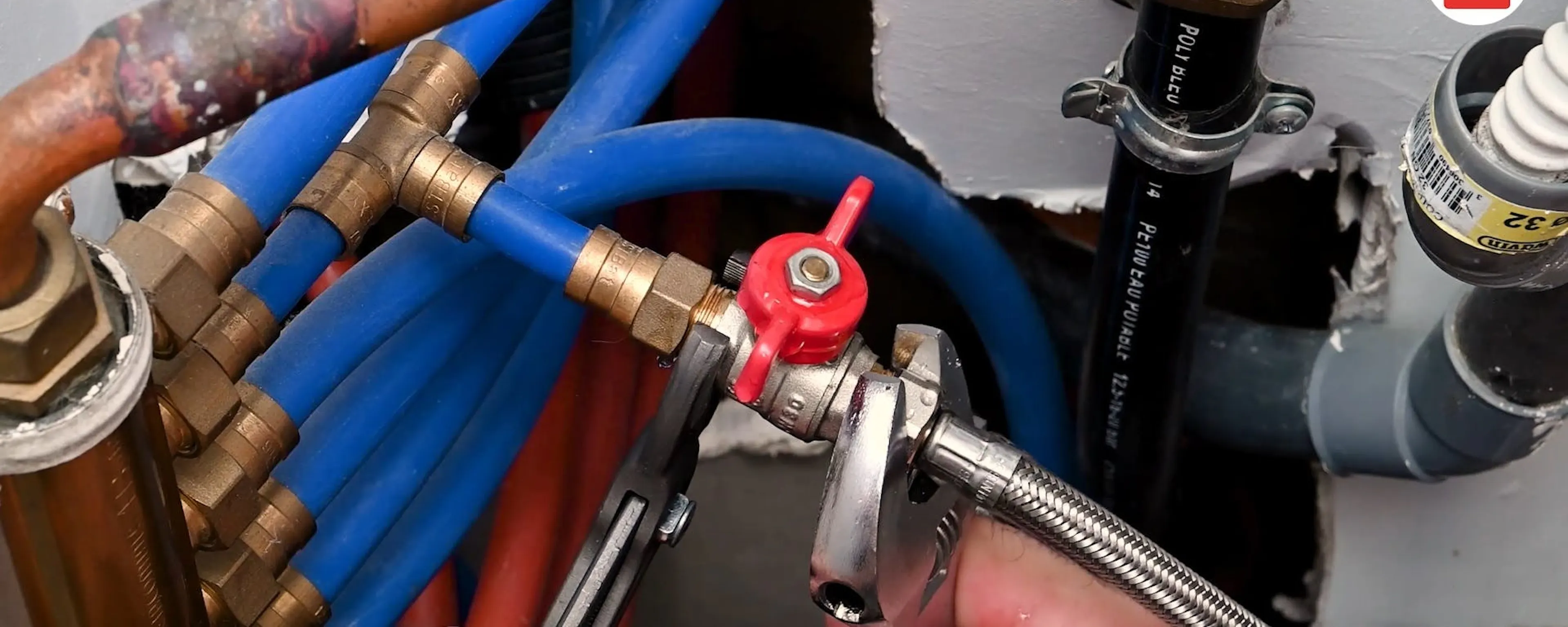 Réseau de tuyaux bleus et cuivrés avec robinet d'arrêt général rouge qui est en train d'être changé