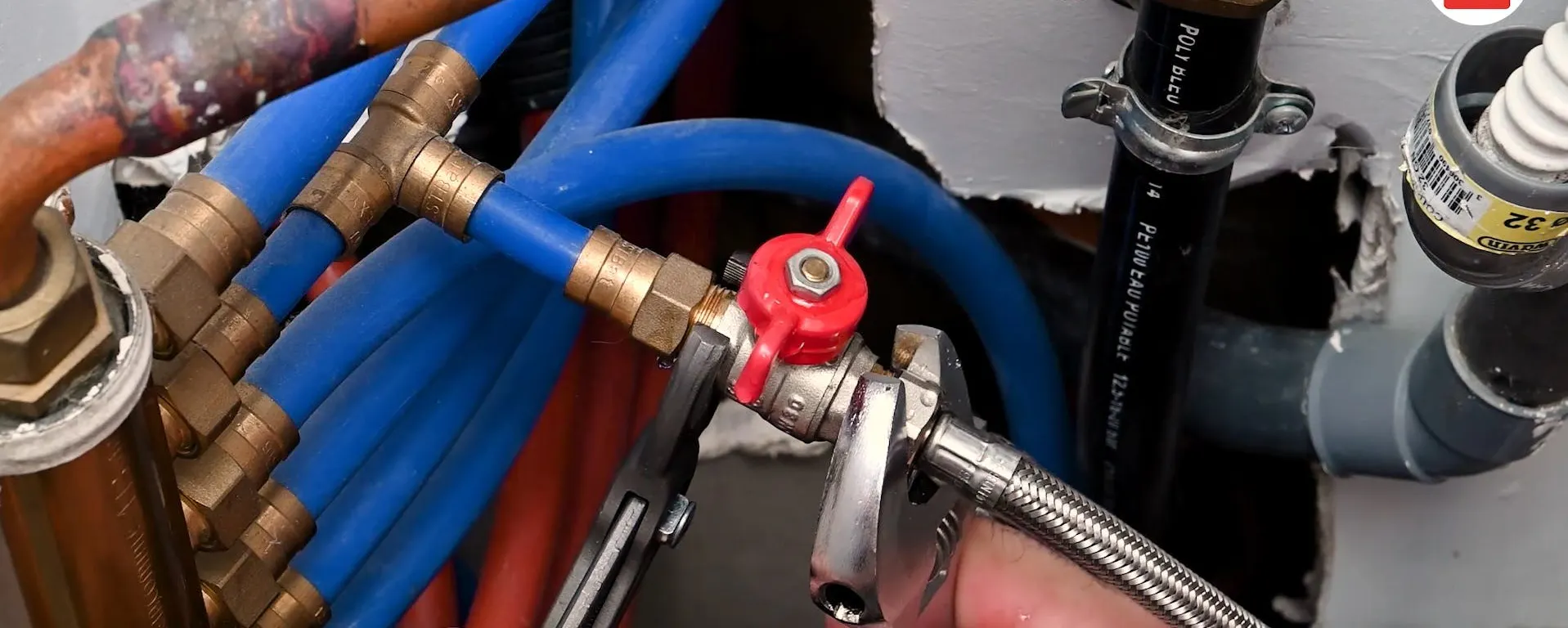 Réseau de tuyaux bleus et cuivrés avec robinet d'arrêt général rouge qui est en train d'être changé