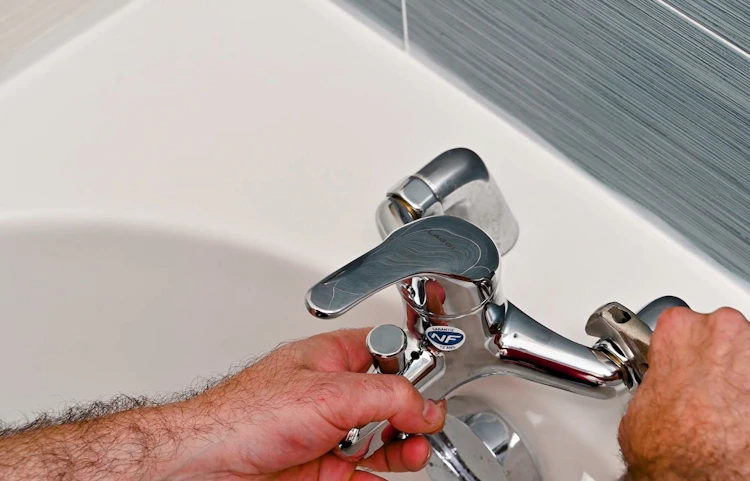 Plombier installant ou réparant un robinet mitigeur sur une baignoire