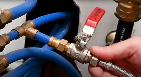 Main manœuvrant une vanne à boisseau sphérique sur tuyaux bleus