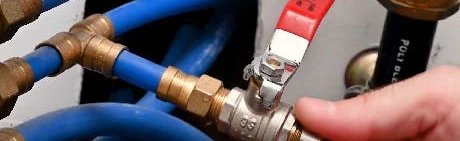 Main manœuvrant une vanne à boisseau sphérique sur tuyaux bleus