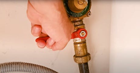 Main fermant un robinet d'arrêt en laiton sur un tuyau flexible