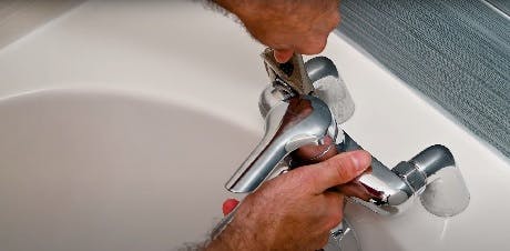 Mains réparant un robinet de lavabo chromé