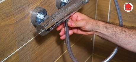 Main tenant le flexible d'un robinet mitigeur de douche chromé