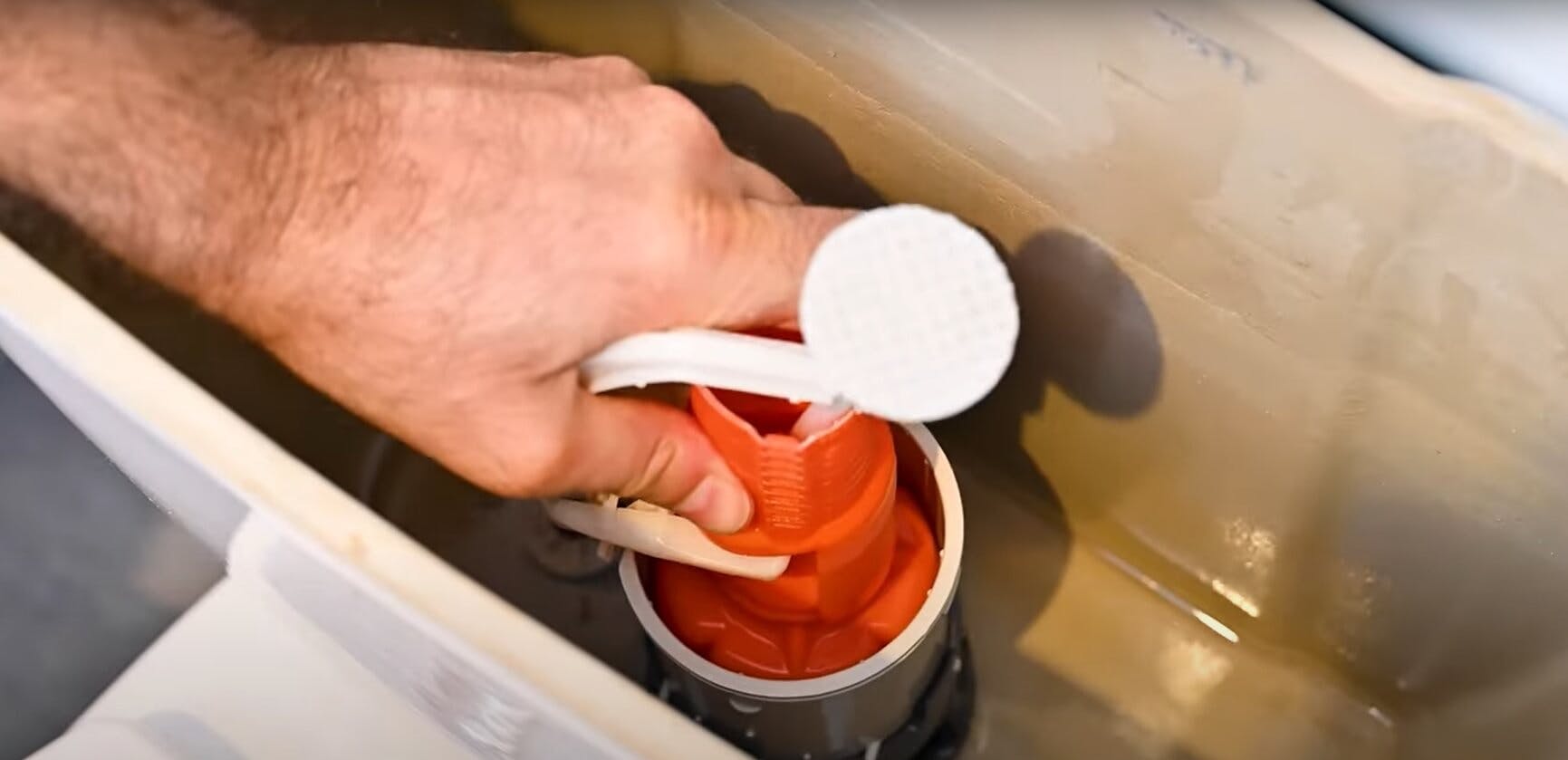 Main tenant le mécanisme de chasse d'eau rouge d'un réservoir de toilettes