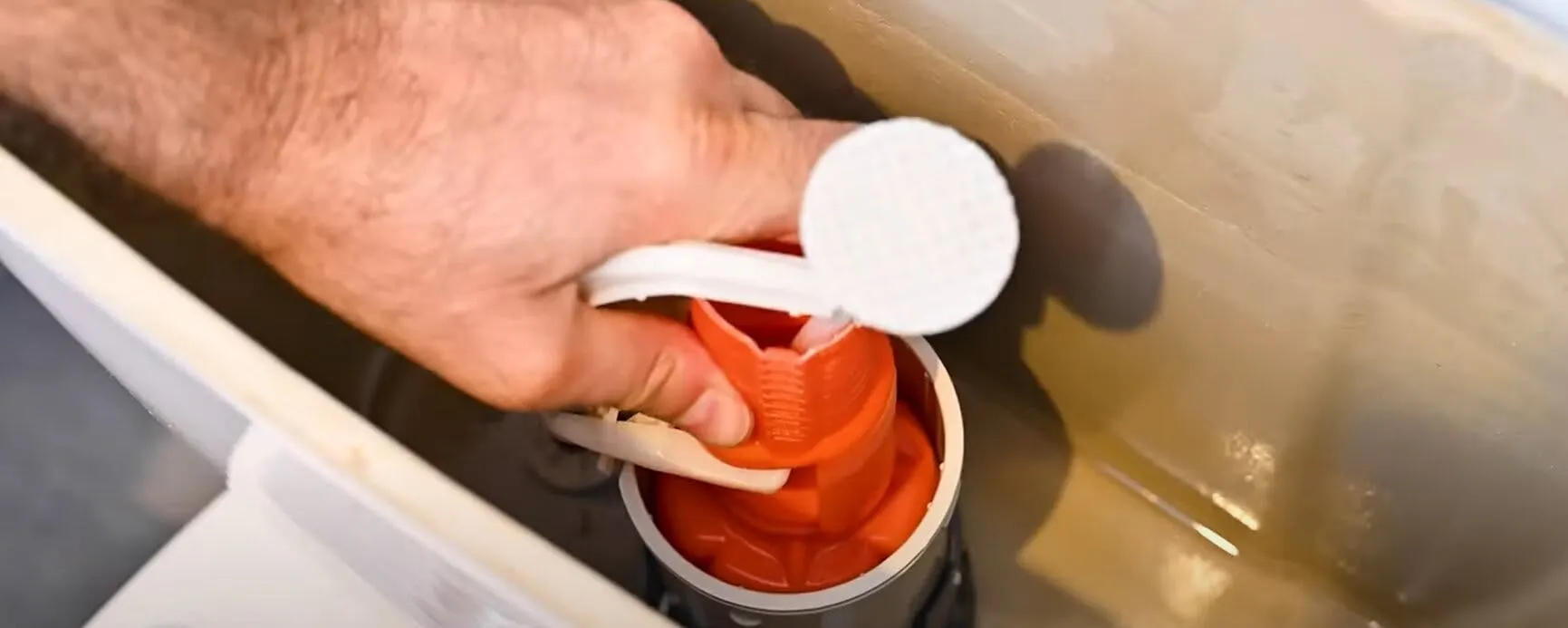 Main tenant le mécanisme rouge d'une chasse d'eau tentant d'économiser l'eau des toilettes