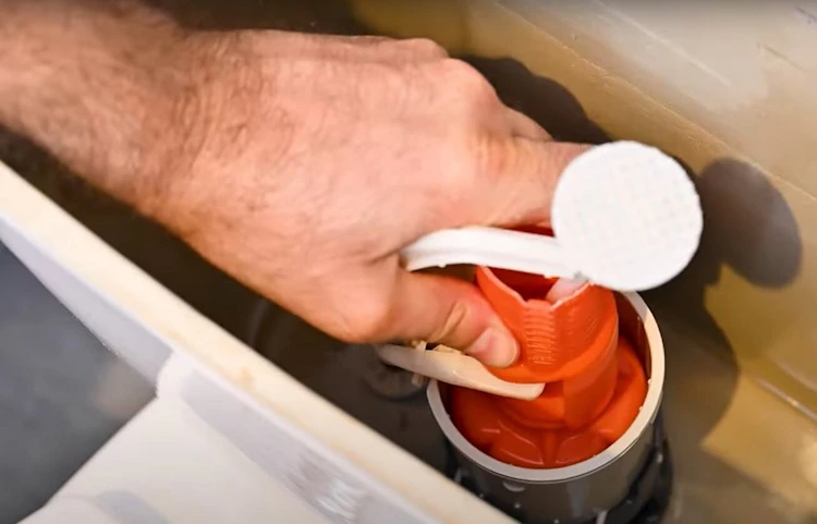 Main tenant le mécanisme de chasse d'eau rouge d'un réservoir de toilettes