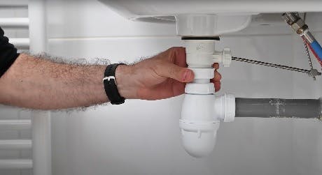 Main serrant le siphon sous un lavabo de salle de bain