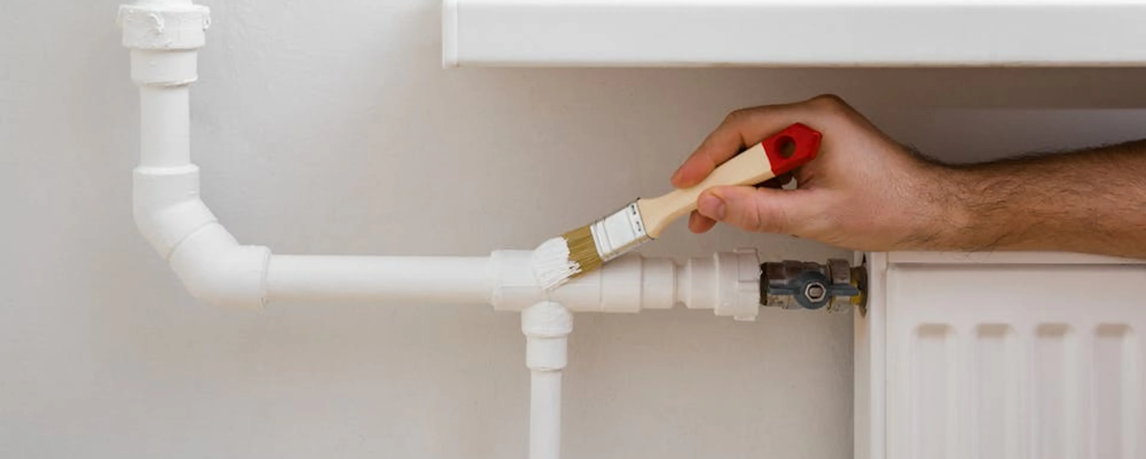 Main peignant la tuyauterie blanche d'un radiateur mural pour cacher les tuyaux de chauffage