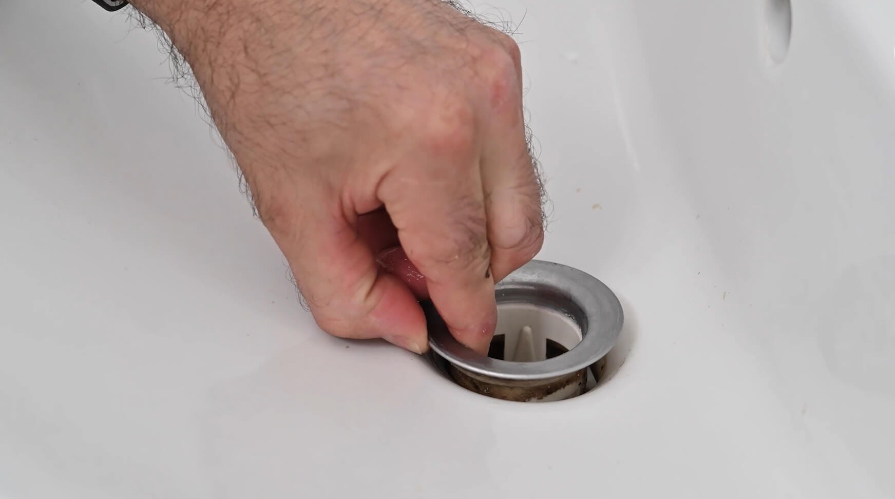 Main retirant la bonde d'un lavabo blanc