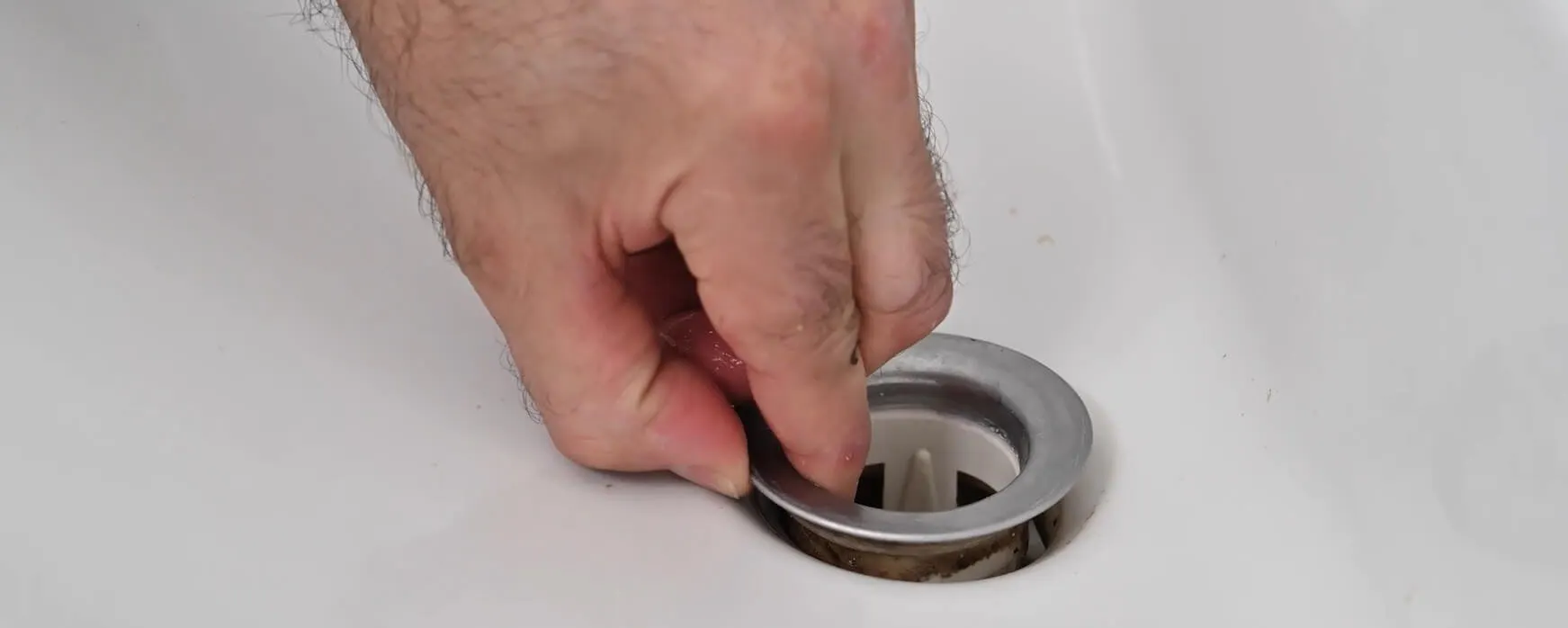 Main retirant la bonde usée d'un lavabo blanc pour la changer